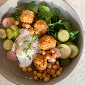 A bowl full of fresh spinach, pickles cucumbers and radishes, chickpeas, white rice, Greek yogurt, and healthy Gluten Free Greek Chicken Meatballs