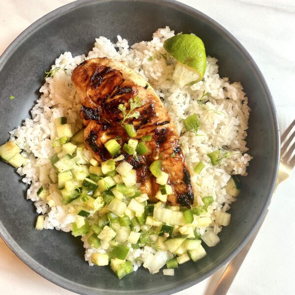 Bowl with white rice topped with grilled pineapple marinated chicken and pineapple salsa with cucumbers, pineapple, green bell peppers, onion, and cilantro. Squeezed lime wedge on the side.