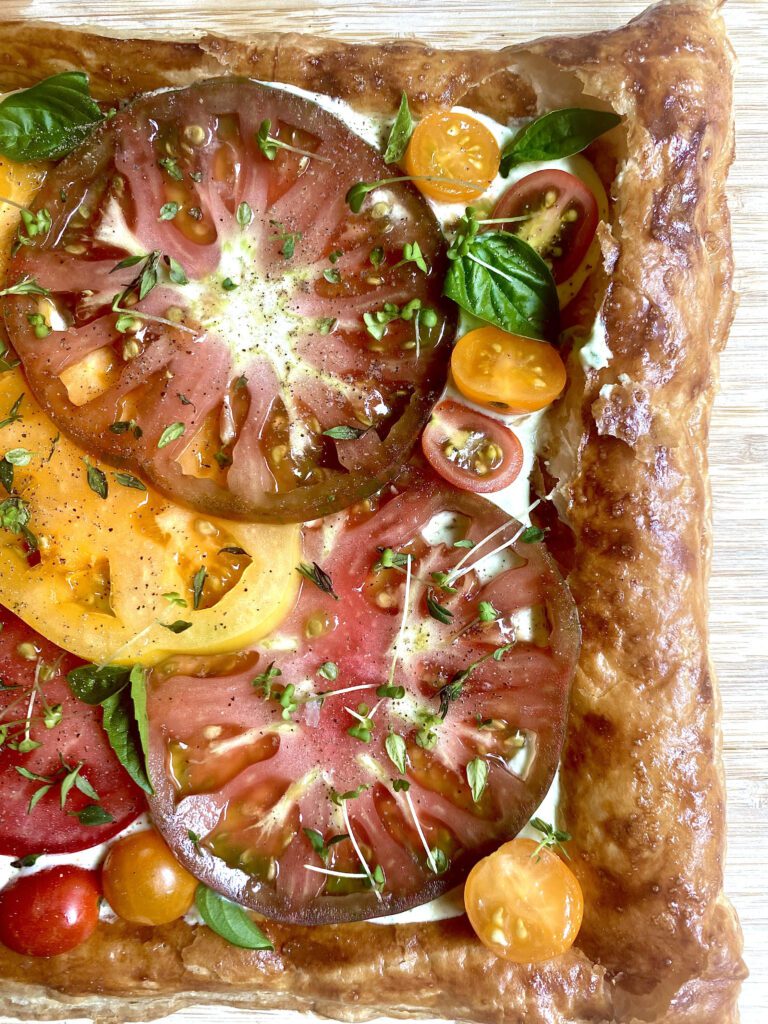 Puff pastry tart filled with fresh heirloom and cherry tomatoes, fresh basil, and microgreens, and a feta basil spread.